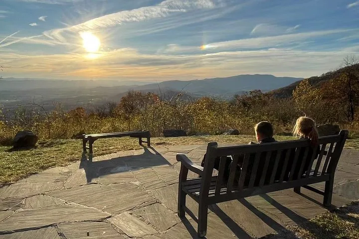 Two people sitting on a bench overlooking a scenic mountain valley at sunset.
